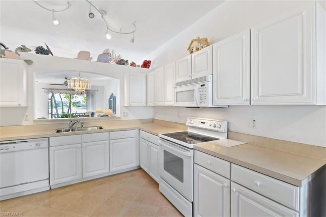 Kitchen featuring white appliances, track lighting, light tile floors, sink, and white cabinetry | Image 15