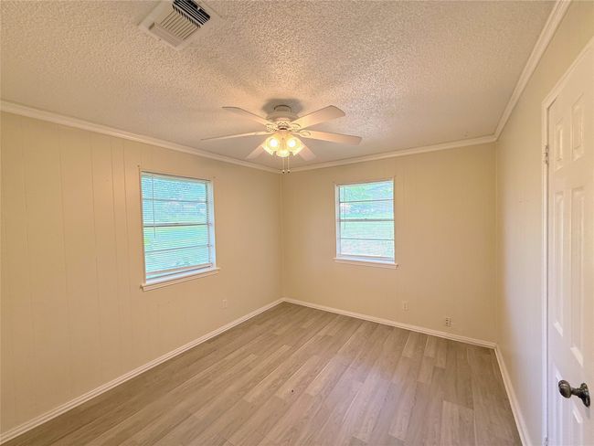 Spare room featuring light wood-type flooring, a textured ceiling, ceiling fan, and ornamental molding | Image 14