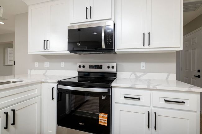 Kitchen with stainless steel appliances, white cabinetry, and light stone counters | Image 19