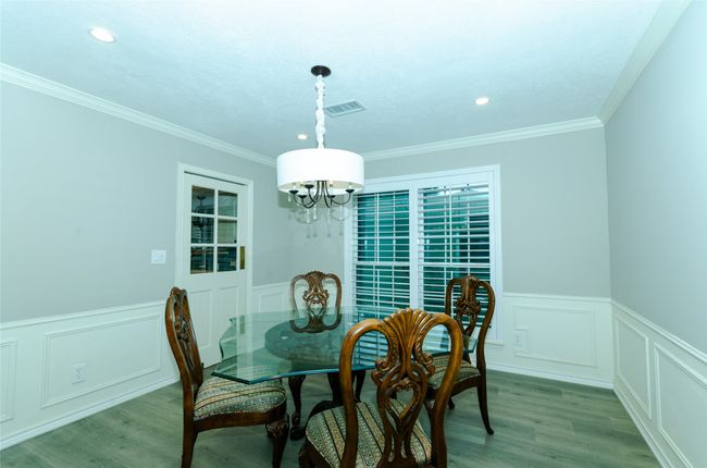 Dining area with a wainscoted wall, wood finished floors, a decorative wall, crown molding, and a chandelier | Image 10
