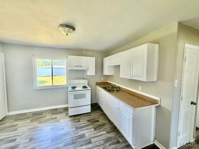 Kitchen with white range with electric cooktop, a sink, under cabinet range hood, white cabinets, and wood finished floors | Image 8