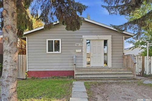 Light gray horizontal siding exterior with a white entry door, an exterior light fixture, and a front porch with wood railings | Card Image