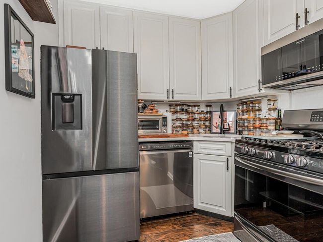 Kitchen with stainless steel appliances, dark wood-style flooring, white cabinetry, and light countertops | Image 10