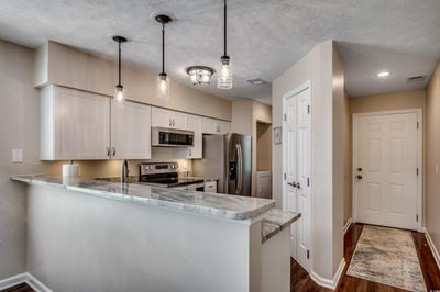 Kitchen featuring stainless steel appliances, white cabinetry, kitchen peninsula, and hanging light fixtures | Image 2