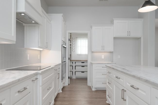 Kitchen featuring white cabinets, custom range hood, black electric stovetop, light wood finished floors, and backsplash | Image 12