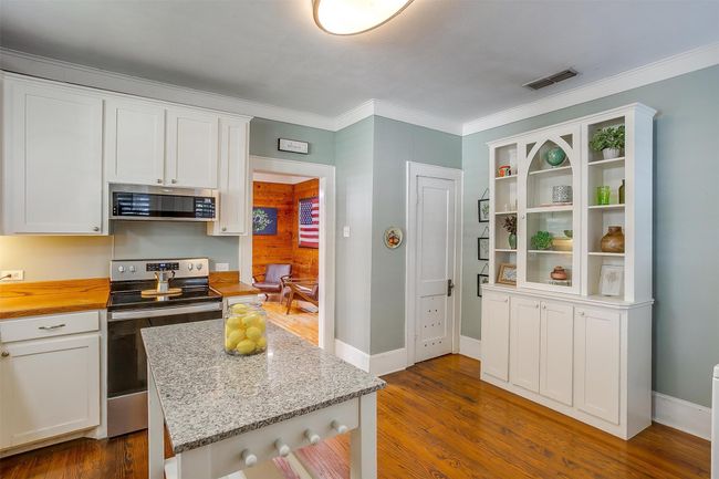 Kitchen featuring stainless steel appliances, white cabinets, dark wood-style floors, ornamental molding, and a kitchen island | Image 23