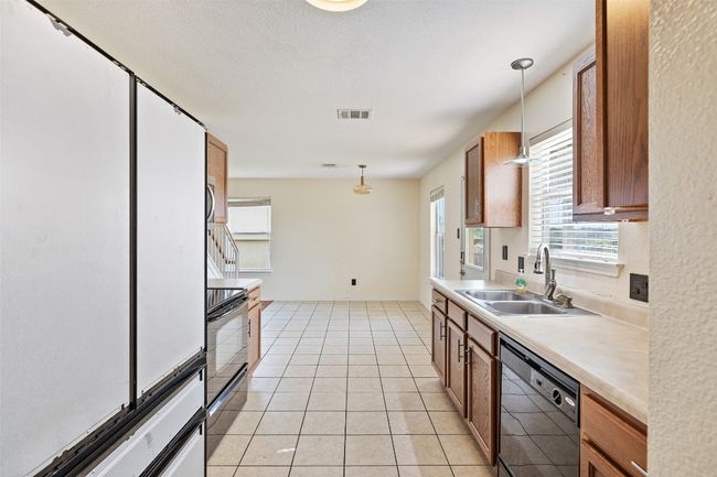 Kitchen with black appliances, a sink, decorative light fixtures, light countertops, and light tile patterned floors | Image 19