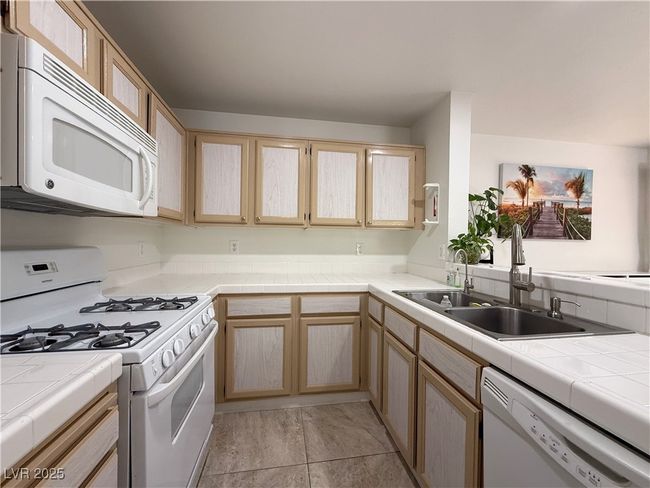 Kitchen with light brown cabinets, tile counters, white appliances, and a sink | Image 22