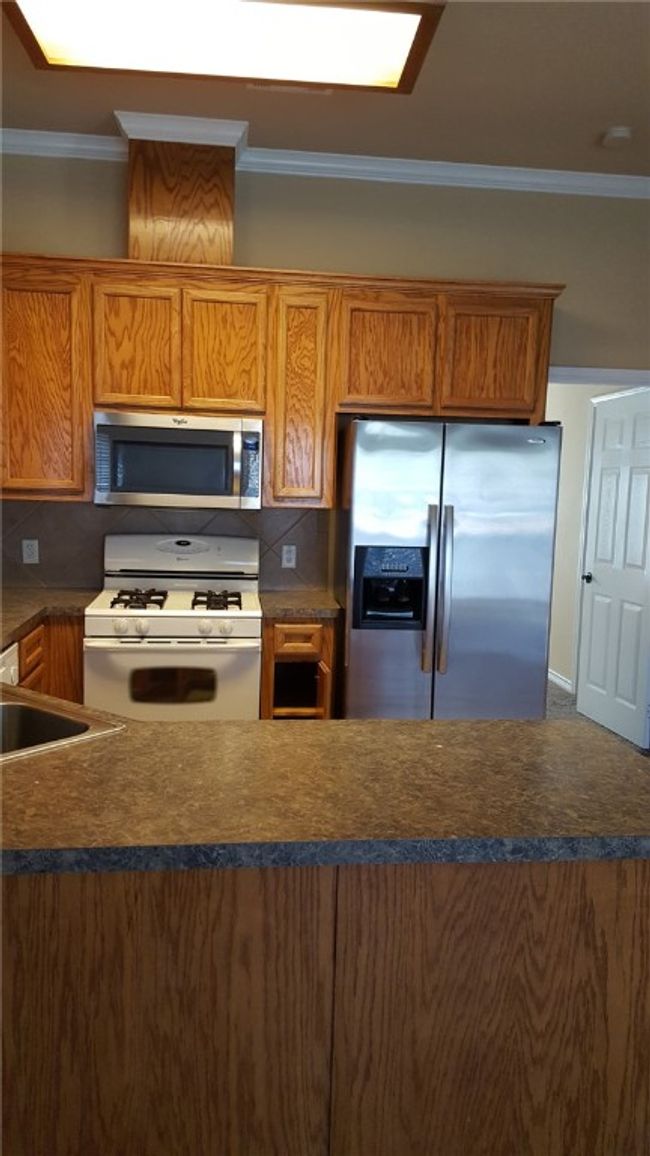 Kitchen featuring appliances with stainless steel finishes, ornamental molding, dark countertops, brown cabinetry, and tasteful backsplash | Image 7