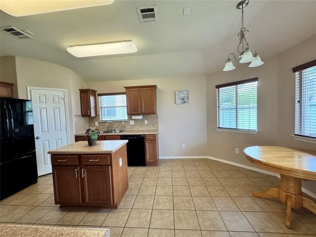 Kitchen featuring black appliances, light countertops, decorative backsplash, light tile patterned floors, and plenty of natural light | Image 9