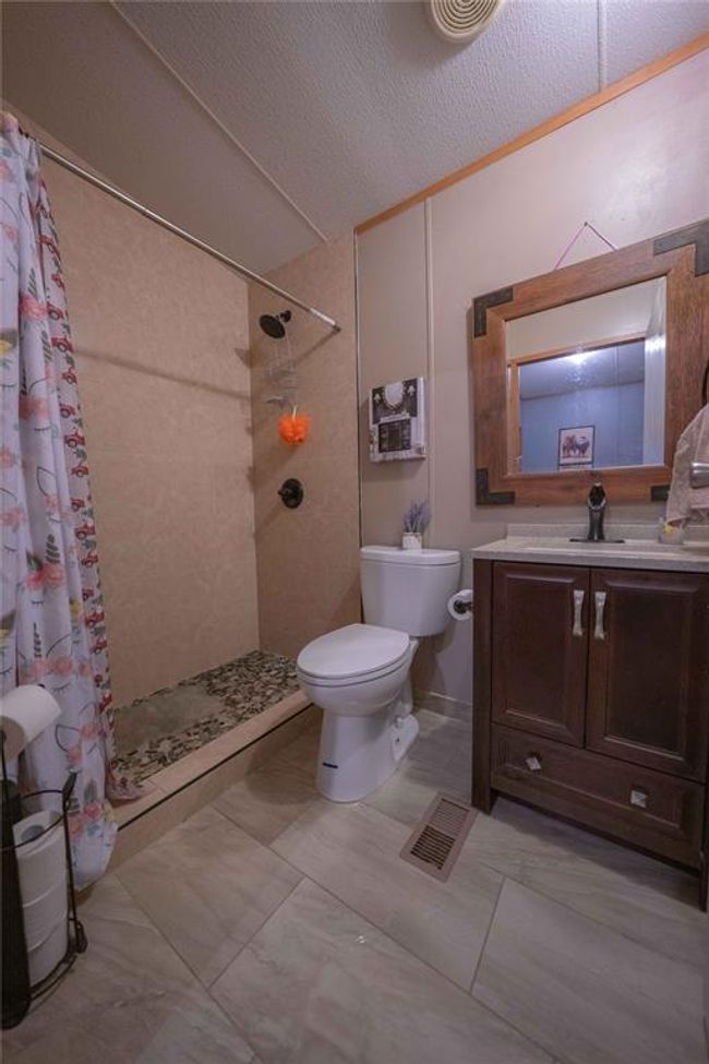 Bathroom with tile flooring, a textured ceiling, curtained shower, toilet, and vanity | Image 24