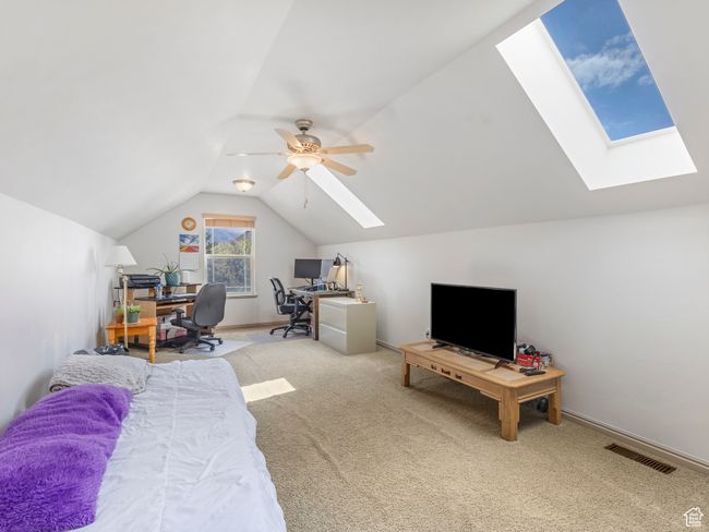 Bedroom featuring a skylight, carpet floors, lofted ceiling, an office area, and a ceiling fan | Image 25