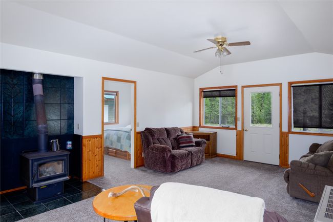 Living room with lofted ceiling, wainscoting, a ceiling fan, a wood stove, and dark carpet | Image 87