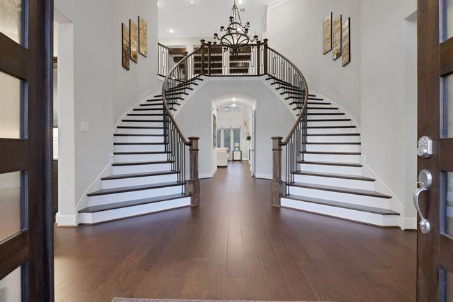 The grand foyer with a stunning double staircase, dark wood flooring, and elegant railings. The space is bright and welcoming, featuring a high ceiling and a central chandelier, creating a luxurious entrance. | Image 8