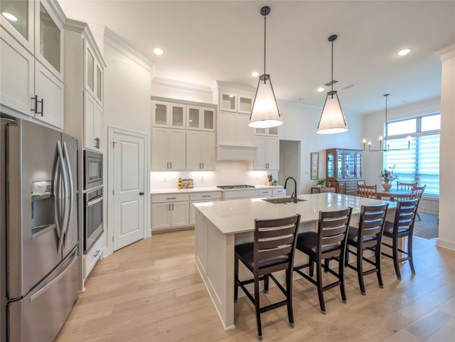 Kitchen with stainless steel appliances, light wood finished floors, an island with sink, light countertops, and a breakfast bar area | Image 10