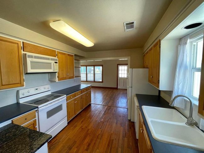 Kitchen with white appliances, dark countertops, dark wood-style flooring, and a sink | Image 5