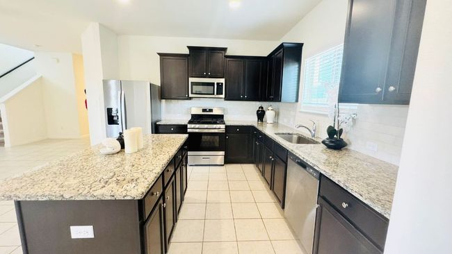 Kitchen featuring backsplash, stainless steel appliances, light tile patterned flooring, a center island, and recessed lighting | Image 19