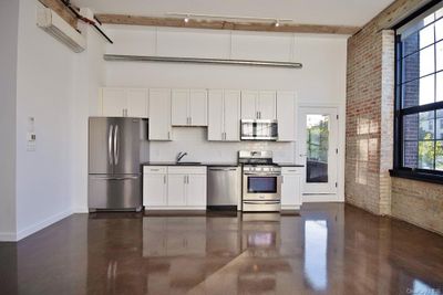 Kitchen featuring brick wall, stainless steel appliances, plenty of natural light, and a high ceiling | Image 3