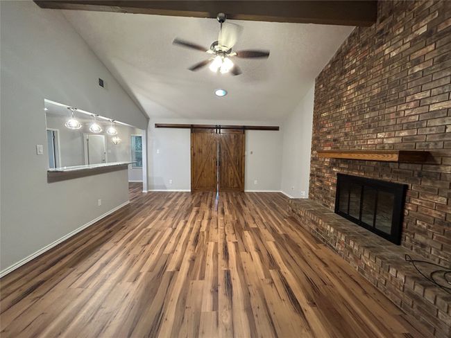 Unfurnished living room featuring vaulted ceiling, a barn door, ceiling fan, wood finished floors, and a fireplace | Image 10