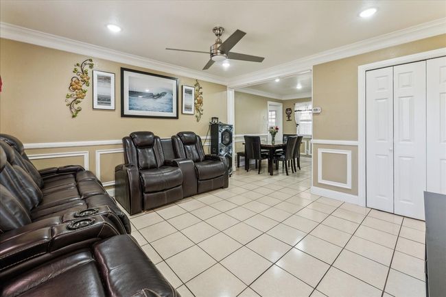 Home theater with light tile patterned flooring, a ceiling fan, wainscoting, a decorative wall, and ornamental molding | Image 17