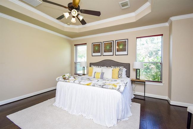 Dark wood floors and soft architectural curves set the tone in the primary bedroom. A tray ceiling and crown molding add depth, while multiple windows ensure a light, tranquil ambiance throughout the day. | Image 18