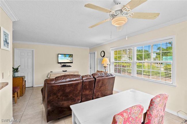 Living room with a textured ceiling, ceiling fan, ornamental molding, and light tile patterned floors | Image 9