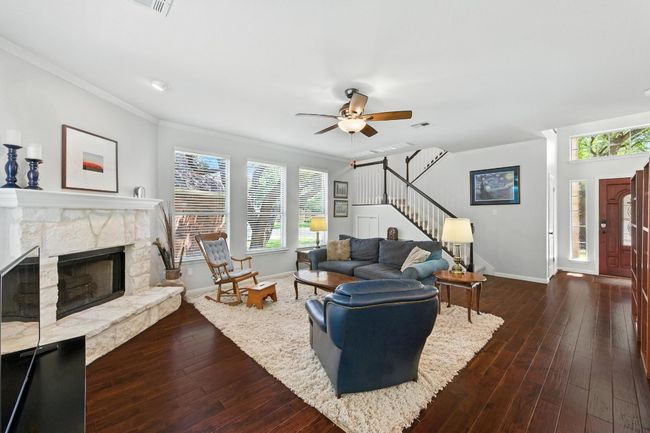 Living area featuring stairs, a ceiling fan, ornamental molding, dark wood finished floors, and a stone fireplace | Image 6
