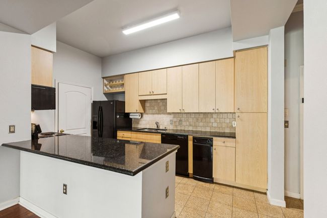 Kitchen with a peninsula, backsplash, black appliances, dark stone counters, and light brown cabinets | Image 15