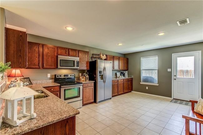 Kitchen with stainless steel appliances, light tile patterned floors, brown cabinetry, recessed lighting, and light stone countertops | Image 7