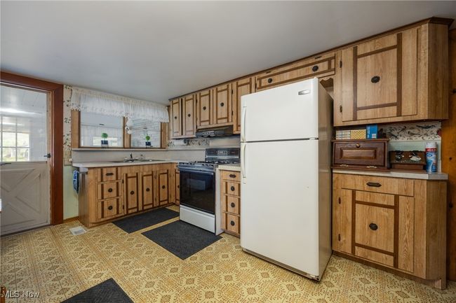 Kitchen featuring freestanding refrigerator, under cabinet range hood, light countertops, a sink, and range with gas cooktop | Image 9
