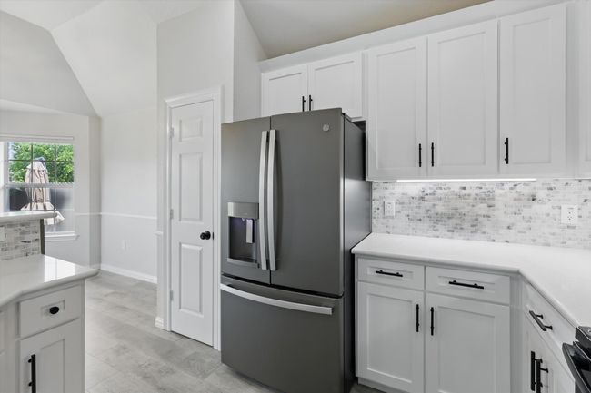 Kitchen with stainless steel refrigerator with ice dispenser, tasteful backsplash, vaulted ceiling, white cabinets, and light countertops | Image 14