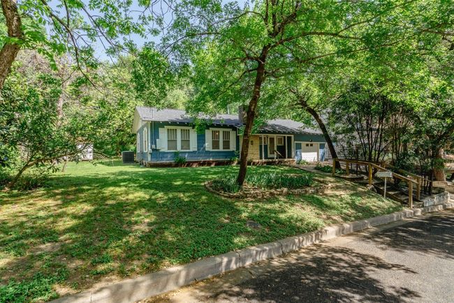 View of front of home featuring a landscaped yard, towering trees, recent HVAC, recent shingled roof, recent water heater and solid oak flooring in living/dining room with high ceilings throughout. 4 bedrooms and 2 full baths. Rock hearth fireplace. | Image 7