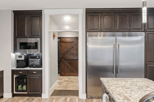 Kitchen featuring built in oversize appliances, dark brown cabinets, and light stone counters | Image 11