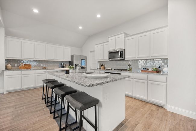 Kitchen featuring appliances with stainless steel finishes, tasteful backsplash, light wood-type flooring, a center island with sink, and lofted ceiling | Image 5