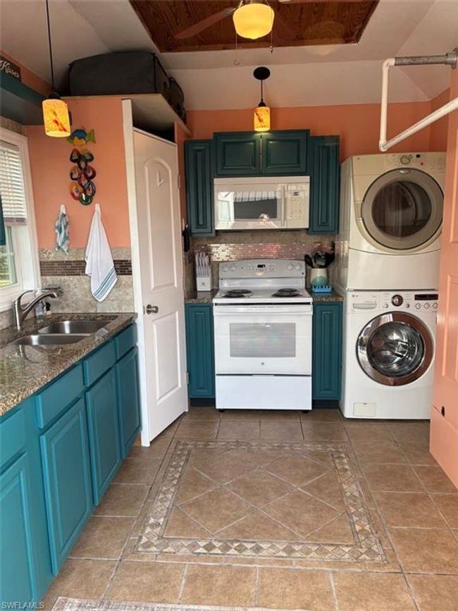 Kitchen featuring a sink, tasteful backsplash, white appliances, blue cabinetry, and stacked washer / drying machine | Image 15
