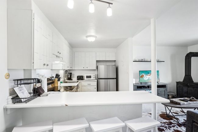 Kitchen featuring a wood stove, a sink, freestanding refrigerator, white microwave, and a peninsula | Image 11