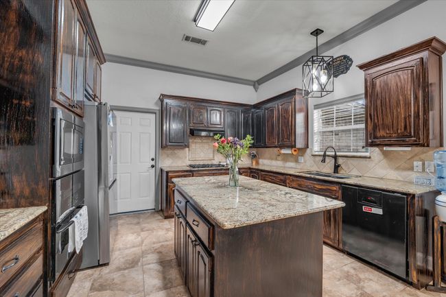 Kitchen with black appliances, a sink, ornamental molding, decorative backsplash, and dark brown cabinetry | Image 10