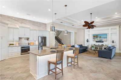 Kitchen featuring appliances with stainless steel finishes, a tray ceiling, white cabinets, a large island with sink, and ceiling fan | Image 2