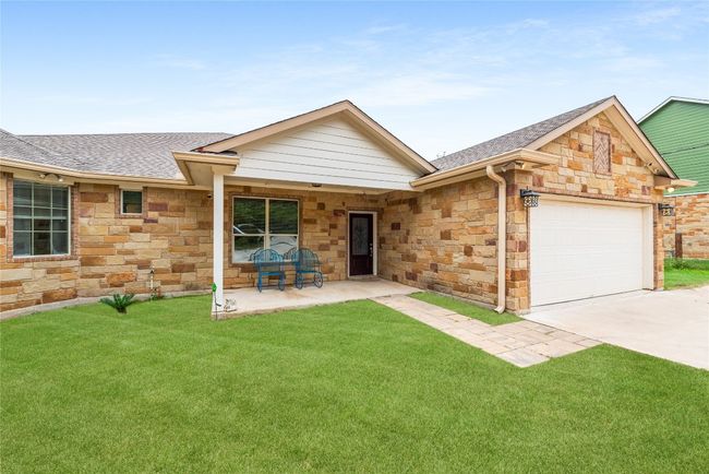 Ranch-style home with stone siding, roof with shingles, an attached garage, driveway, and a front yard | Image 6