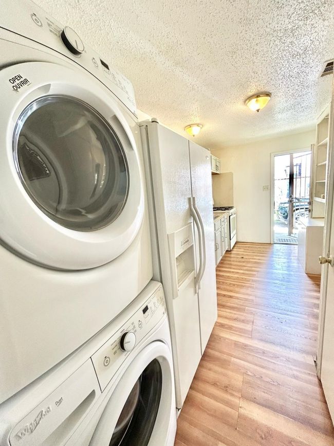 Washroom with stacked washing machine and dryer, a textured ceiling, and light wood-style floors | Image 6