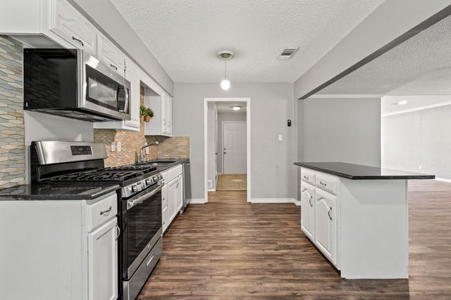 Kitchen with stainless steel appliances, dark countertops, dark wood finished floors, a sink, and a textured ceiling | Image 6