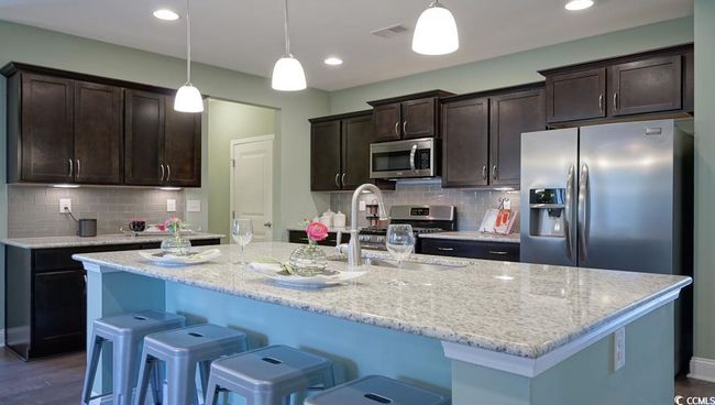 Kitchen featuring appliances with stainless steel finishes, a sink, dark brown cabinetry, a center island with sink, and tasteful backsplash | Image 5