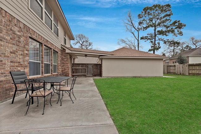 This photo showcases a spacious backyard with a well-maintained lawn and a concrete patio area. There's a brick exterior house wall with several windows and a seating area with a table and chairs, perfect for outdoor dining or relaxing. The yard is fenced, providing privacy and security. | Image 4