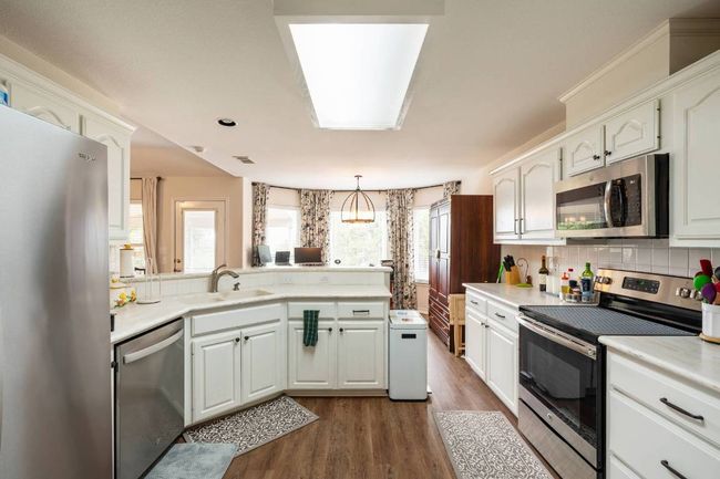 Kitchen featuring dark wood finished floors, a sink, decorative backsplash, a peninsula, and appliances with stainless steel finishes | Image 21