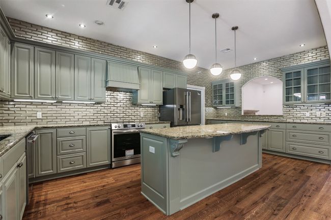 Kitchen with stainless steel appliances, glass insert cabinets, tasteful backsplash, a breakfast bar, and recessed lighting | Image 5