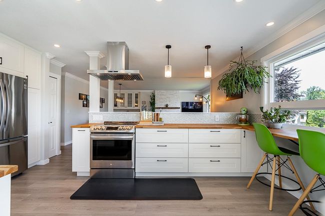 Kitchen with stainless steel appliances, wooden counters, island range hood, ornamental molding, and backsplash | Image 13