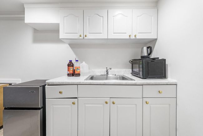 Kitchen with a sink, black microwave, light countertops, white cabinetry, and freestanding refrigerator | Image 28