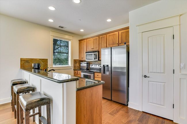 Kitchen finishes, brown cabinetry, receessedlighting, decorative backsplash, and light wood-type flooring, breakfast Bar and pantry. | Image 8