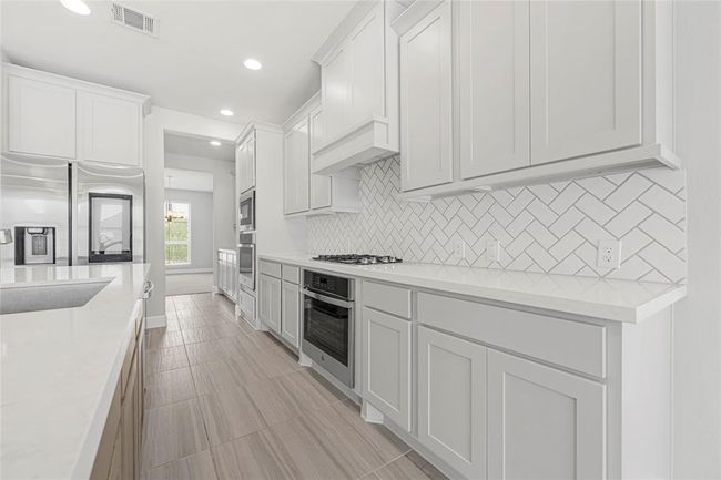 Modern cabinetry and backsplash. Quartz countertops. There are two ovens and a butler pantry in the kitchen. Beautiful mantel hood. Built-in microwave. | Image 10