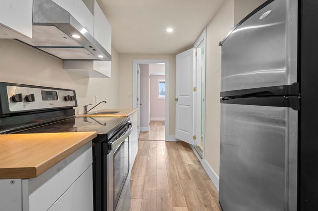 Kitchen with wall chimney range hood, a sink, white cabinetry, appliances with stainless steel finishes, and recessed lighting | Image 14